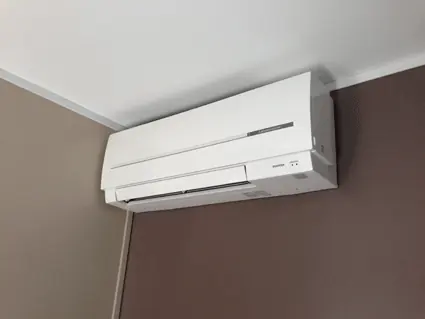Unité intérieure murale posée dans l'angle d'une chambre, entre un mur blanc et un mur peint en brun.