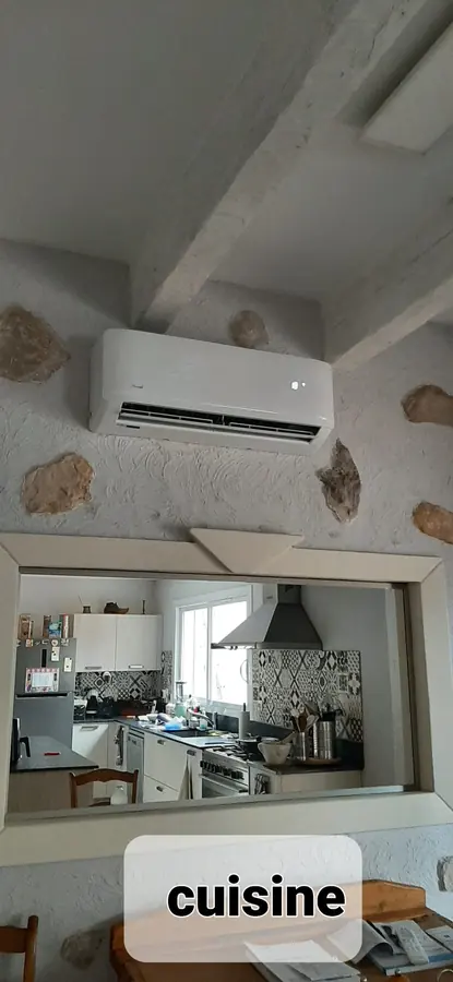 Unité intérieure murale posée sous un plafond à poutres, au-dessus de l'ouverture sur la cuisine.