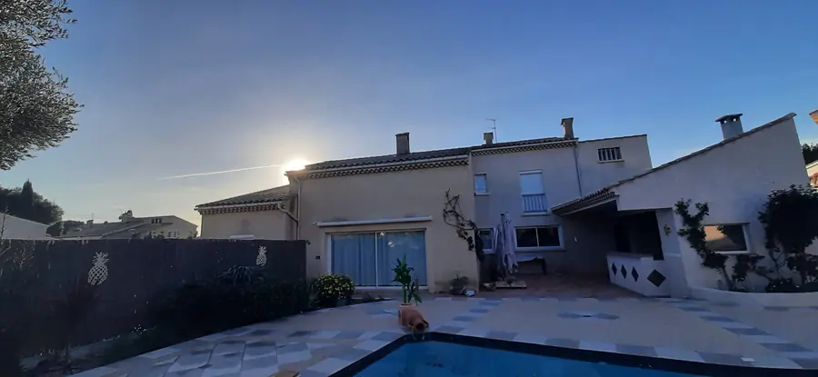 Vue d'ensemble de la villa équipée, au crépuscule, la piscine au premier plan.