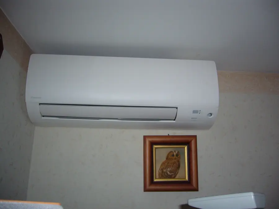 Unité intérieure murale blanche Daikin fixée en haut d'un mur beige, au-dessus d'un petit tableau encadré.