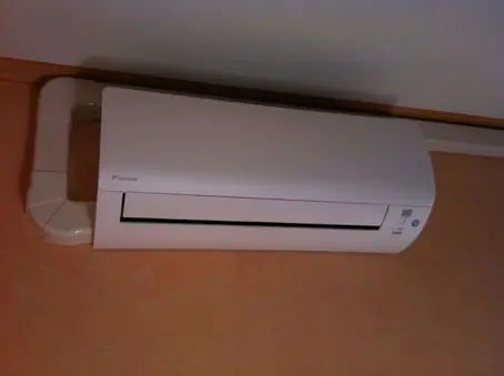Unité intérieure murale Daikin posée sous une poutre, sur le mur ocre d'une chambre d'enfant.
