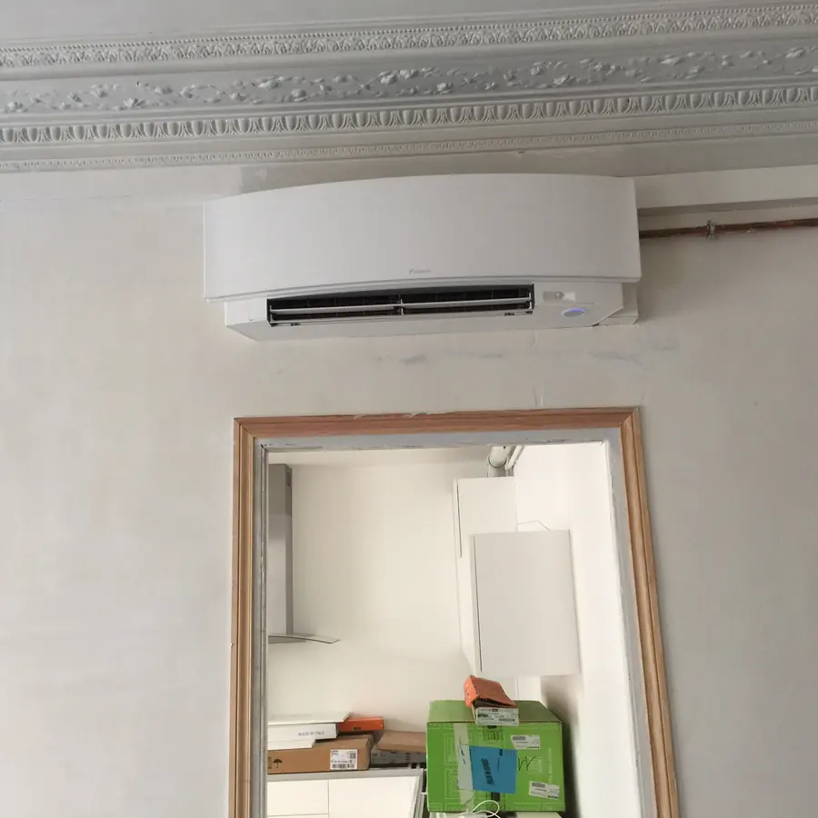Unité intérieure murale posée au-dessus d'une porte, sous la corniche moulurée d'un appartement niçois.