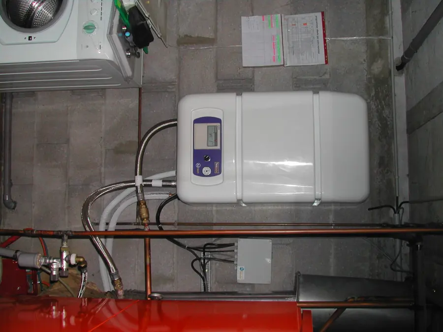 Module intérieur de la pompe à chaleur air-eau dans le local technique, raccordements cuivre apparents au-dessus du ballon.