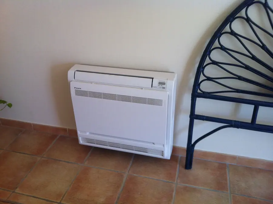 Console au sol Daikin FVXS35F posée contre le mur d'une chambre, à côté d'une tête de lit en fer forgé.