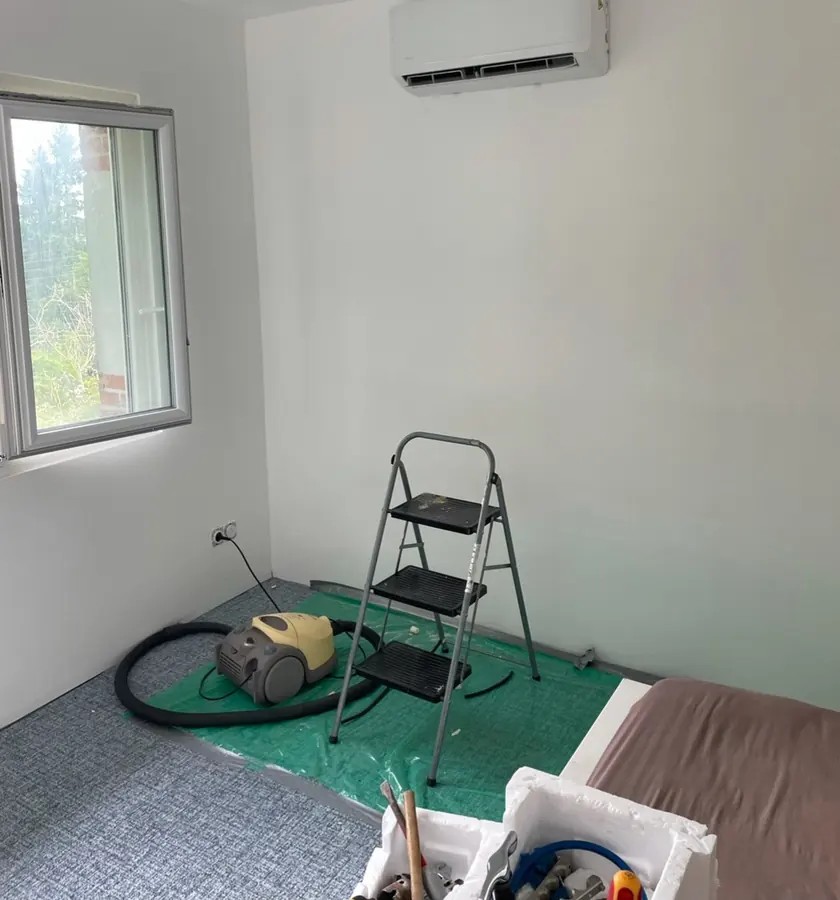 Chambre en cours d'équipement : unité intérieure murale posée en haut du mur, sol protégé par une bâche pendant l'intervention.