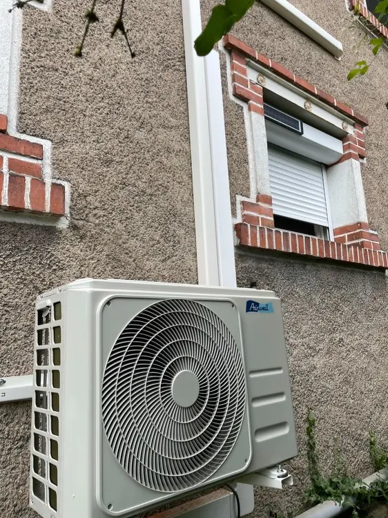 Unité extérieure Airwell fixée sur consoles contre une façade en crépi à encadrements de briques rouges.
