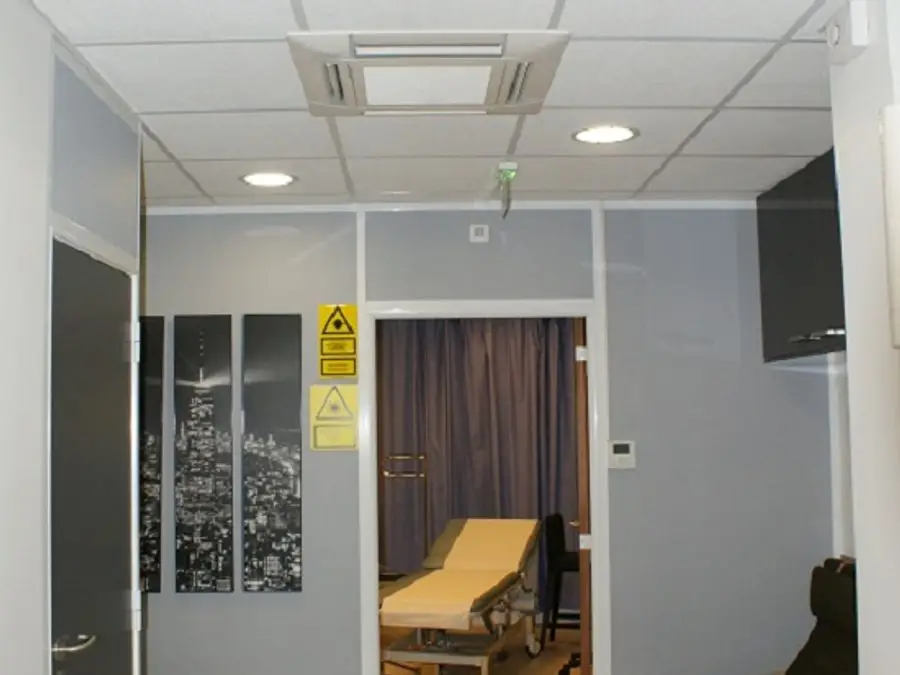 Couloir de cabinet médical climatisé par une cassette encastrée dans le faux plafond, devant une salle d'examen.