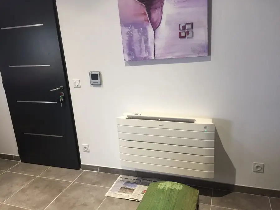 Console de climatisation réversible posée au sol le long d'un mur d'entrée, à la place d'un radiateur.