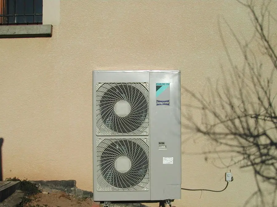 Groupe extérieur bi-ventilateur d'une pompe à chaleur air-eau Daikin, posé sur plots au pied d'une façade.