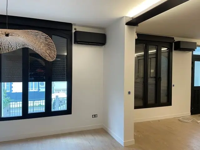 Séjour entièrement rénové : deux unités intérieures murales noires posées au-dessus des menuiseries, dans une pièce à parquet clair.